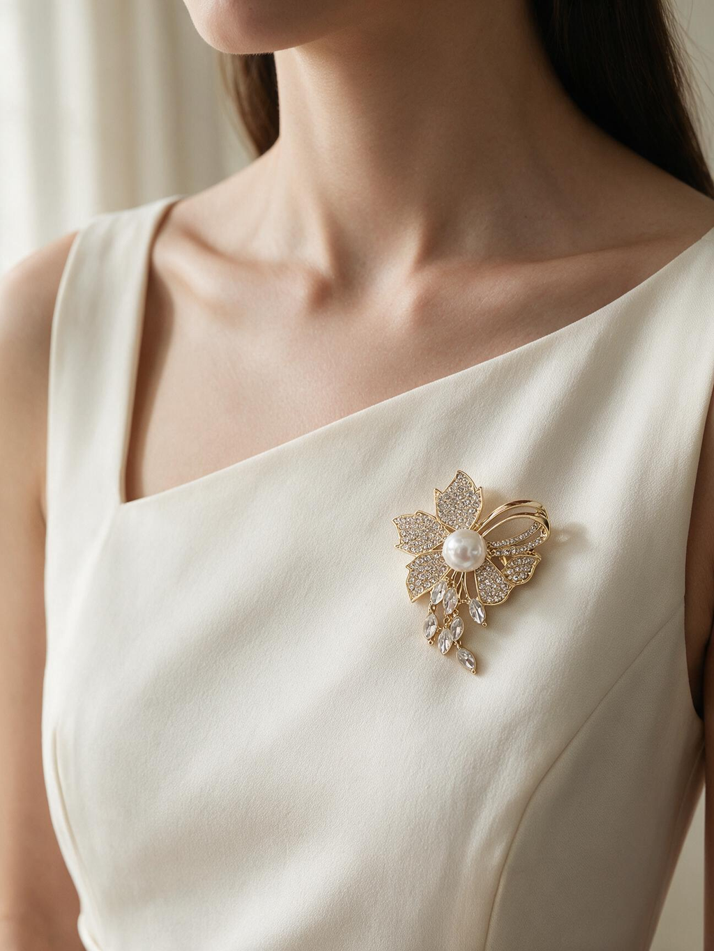 Gold-tone floral brooch with a pearl-look center and dangling clear stones worn on an ivory dress